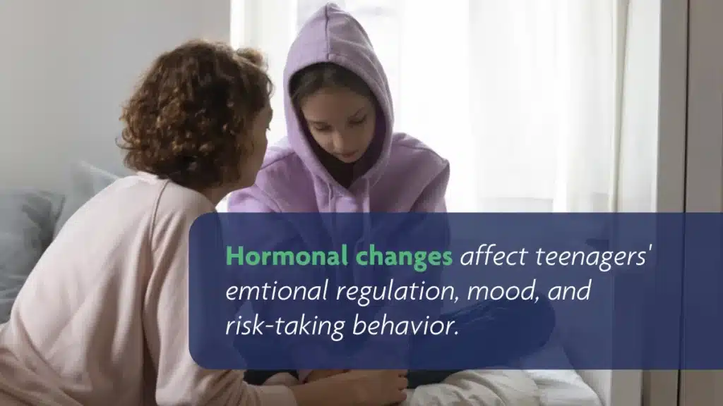 Teen girl in a purple hoodie sitting on a couch while talking to her mom. Hormonal changes affect teenagers’ emotional regulation.