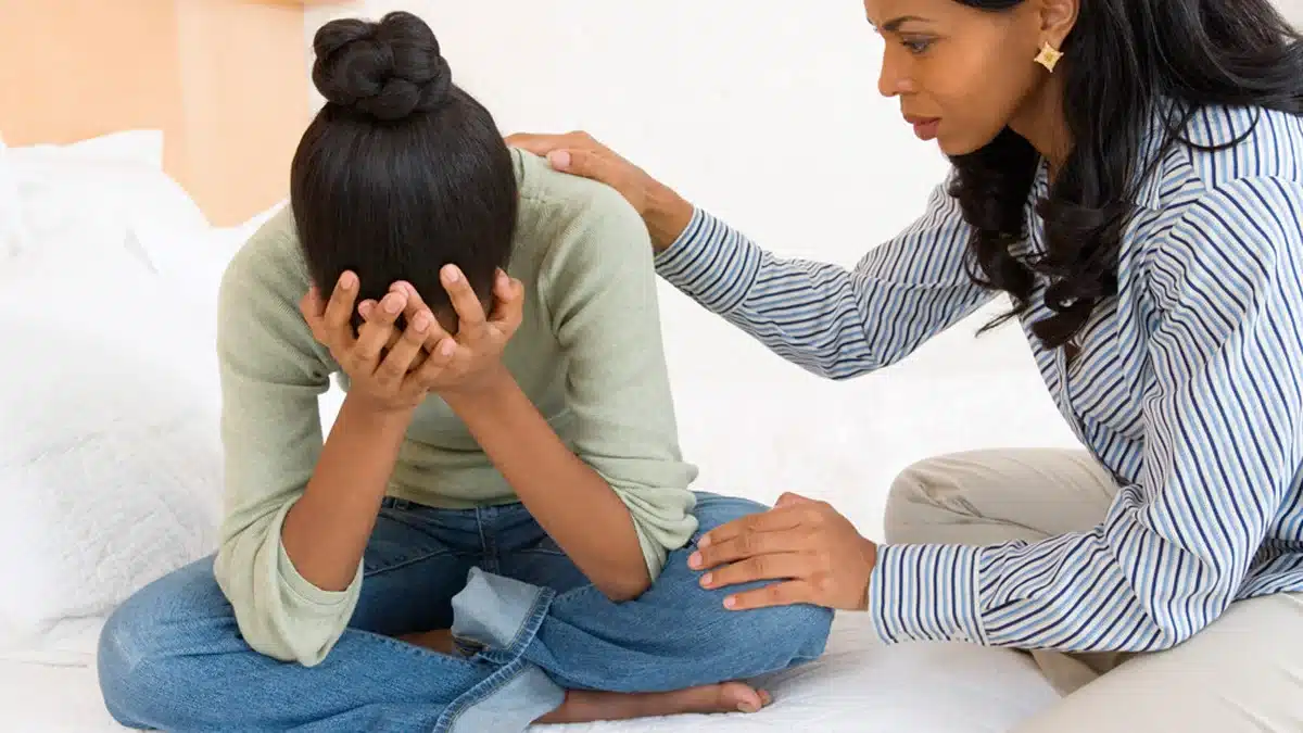 Teenager with her head in her hands while her mother comforts her.