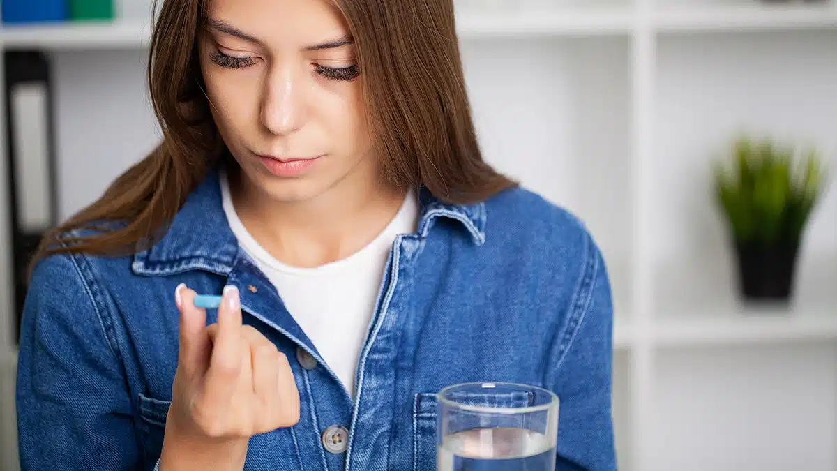 Teenager holding a blue pill between her fingers.