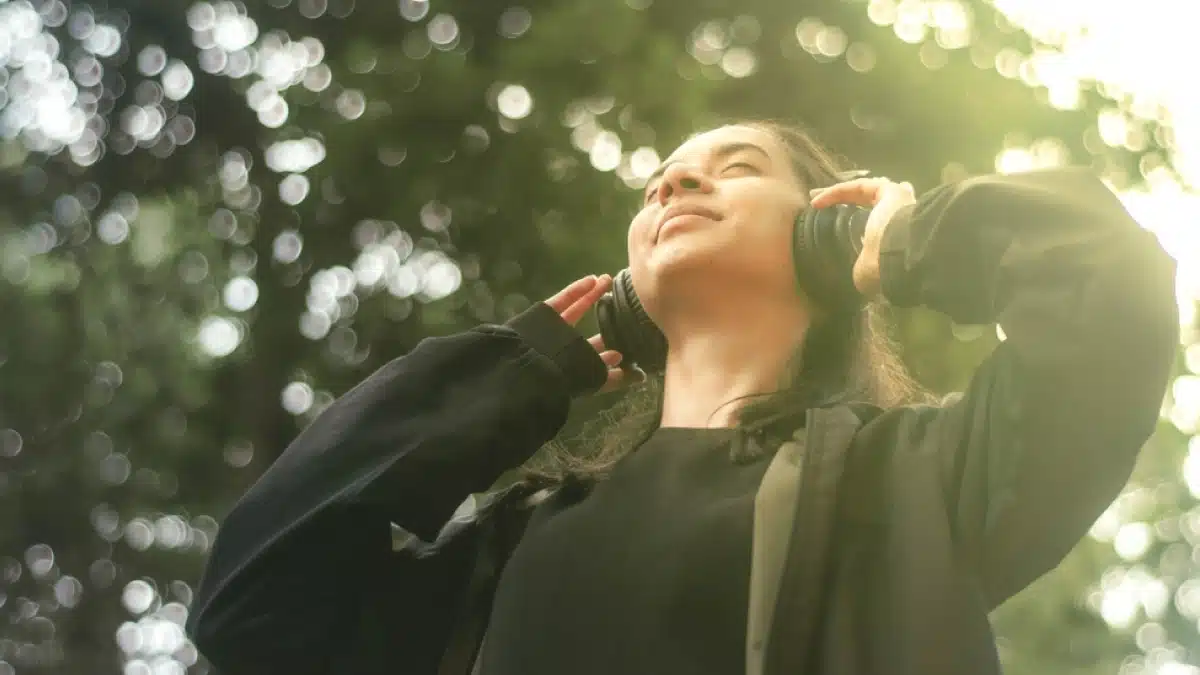 Teenager in the forest wearing large headphones. Blue text on white background explains how music therapy enhances brain activity.